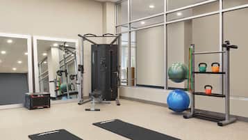 A gym with exercise equipment, black mats, and a kettlebell rack.