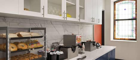 A kitchen with a marble backsplash, a glass display case with pastries, a coffee machine, and a window with stained glass.