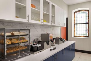 Une cuisine avec un pare-feu en marbre, une vitrine en verre où sont exposées des pâtisseries, une machine à café et une fenêtre ornée de vitraux.