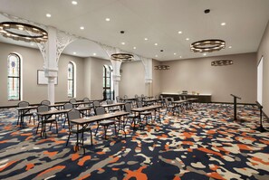 Une salle de conférence équipée de tables et de chaises, de grandes fenêtres et d’un tapis à motifs.