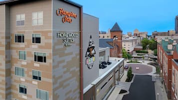A Hampton Inn hotel with Homewood Suites by Hilton, featuring a modern design with a mix of beige and gray tones, multiple windows, and a prominent logo.