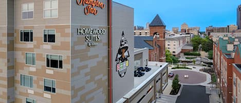 A Hampton Inn hotel with Homewood Suites by Hilton, featuring a modern design with a mix of beige and gray tones, multiple windows, and a prominent logo.