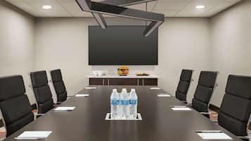 Sala de conferência com uma mesa comprida, cadeiras pretas, garrafas de água e uma tela de projetor.