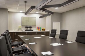 Une salle de conférence avec une longue table, des chaises noires, un tableau blanc et un coin café.