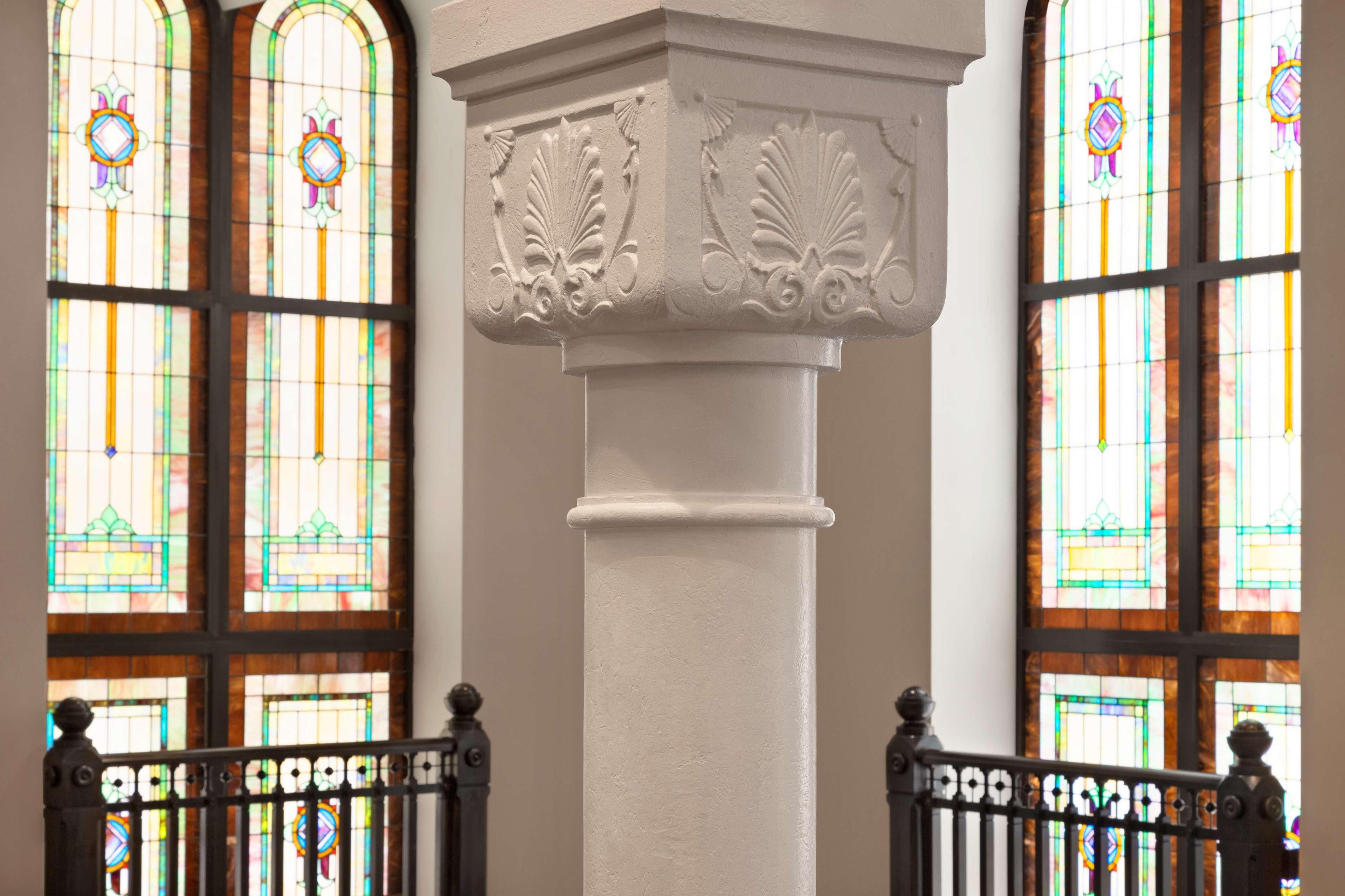 A white column with ornate carvings, flanked by two stained glass windows with colorful patterns.