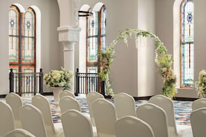 Een kerkinterieur met banken, glas-in-loodramen en bloemversiering.