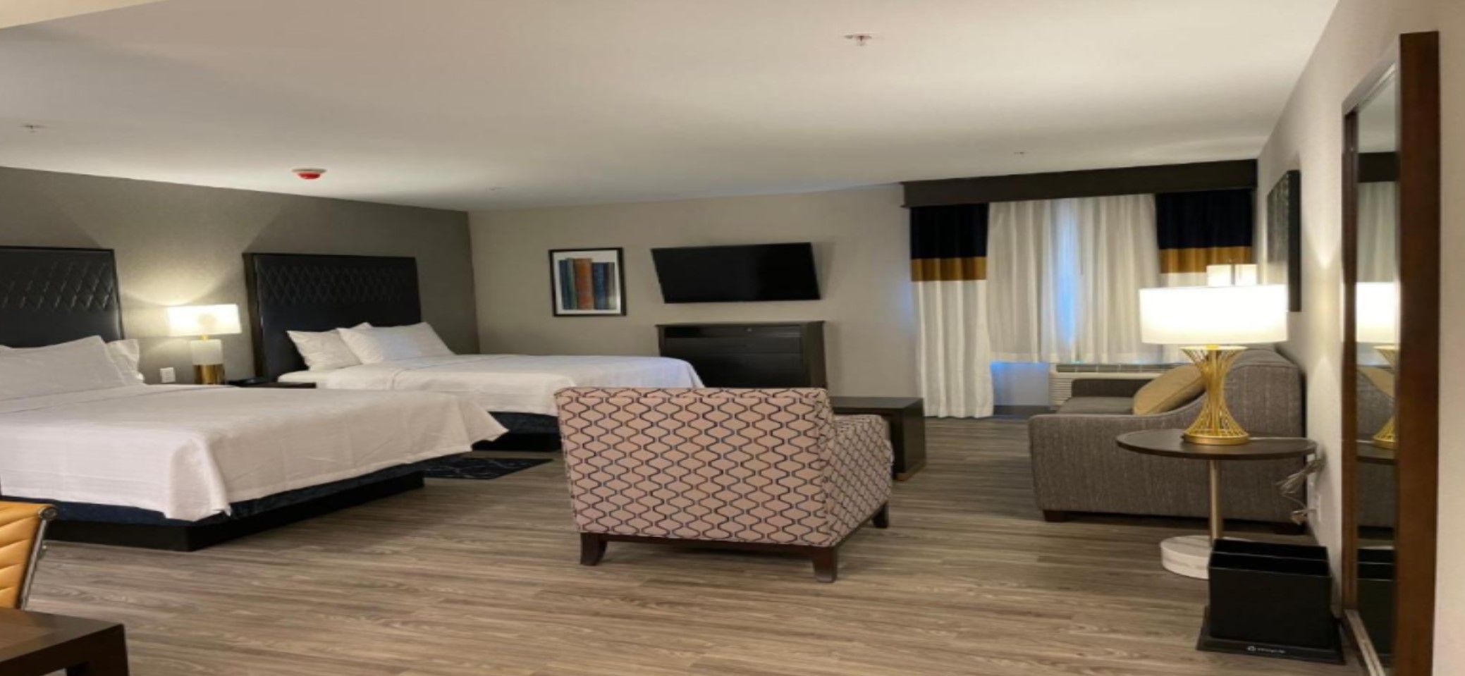 Una habitación de hotel con dos camas, un sofá, un escritorio, un televisor y una lámpara.