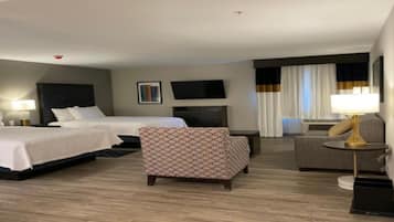 Una habitación de hotel con dos camas, un sofá, un escritorio, un televisor y una lámpara.
