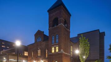 A historic brick building with a prominent tower and arched windows, surrounded by modern structures.