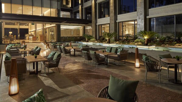 Un patio exterior con diversas zonas de estar, una fuente de agua y una entrada bien iluminada.