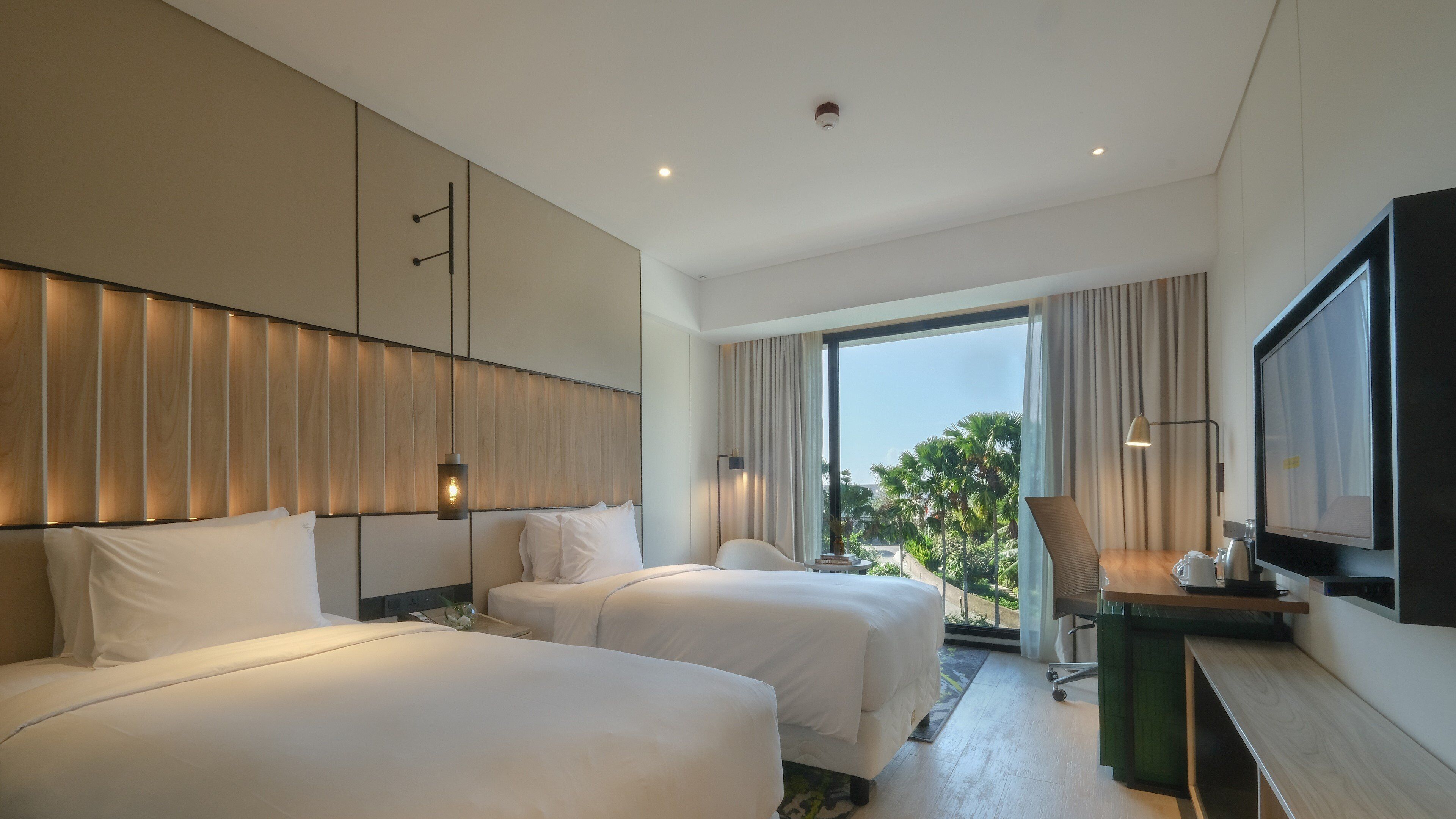 A hotel room with two beds, a TV, a desk, and a view of palm trees.