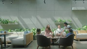 Un grupo de personas sentadas alrededor de una mesa en un espacio al aire libre moderno y bien iluminado, con plantas en macetas y mobiliario de mimbre.