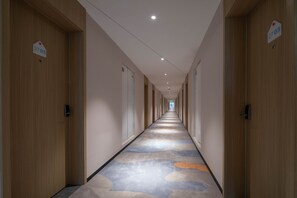 En lång, smal hotellkorridor med trädörrar på båda sidor, numrerade skyltar ovanför varje dörr och en mönstrad matta.