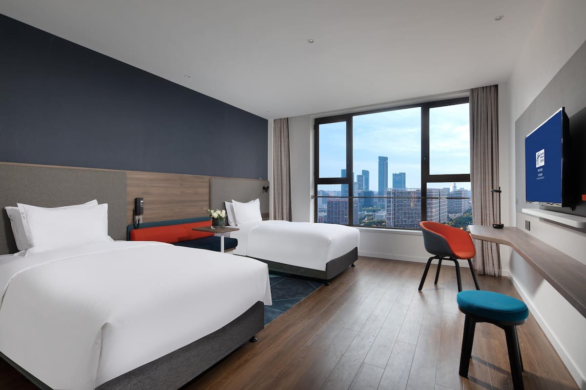 A hotel room with two beds, a desk, a chair, and a TV.