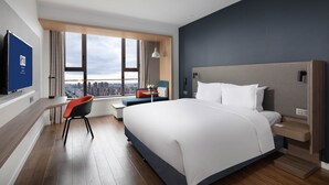 Ein modernes Hotelzimmer mit einem großen Bett, einem Schreibtisch, einem Stuhl und Blick auf die Stadt.