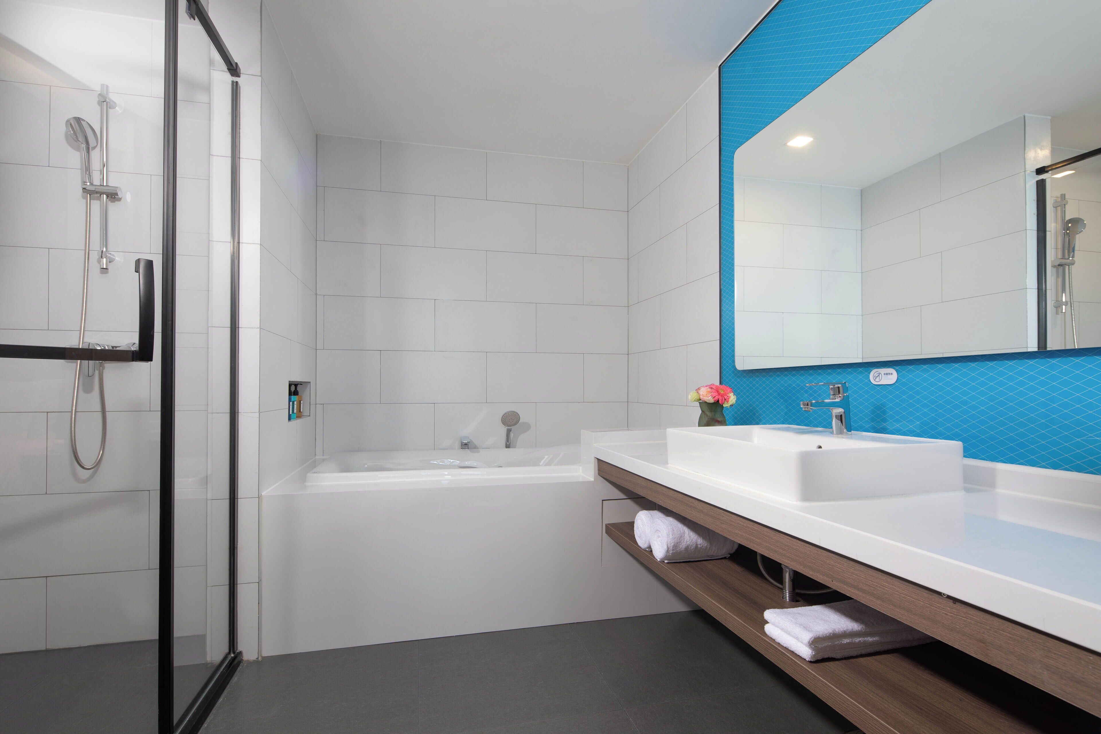 A modern bathroom with a glass-enclosed shower, a white bathtub, and a vanity with a mirror and sink.