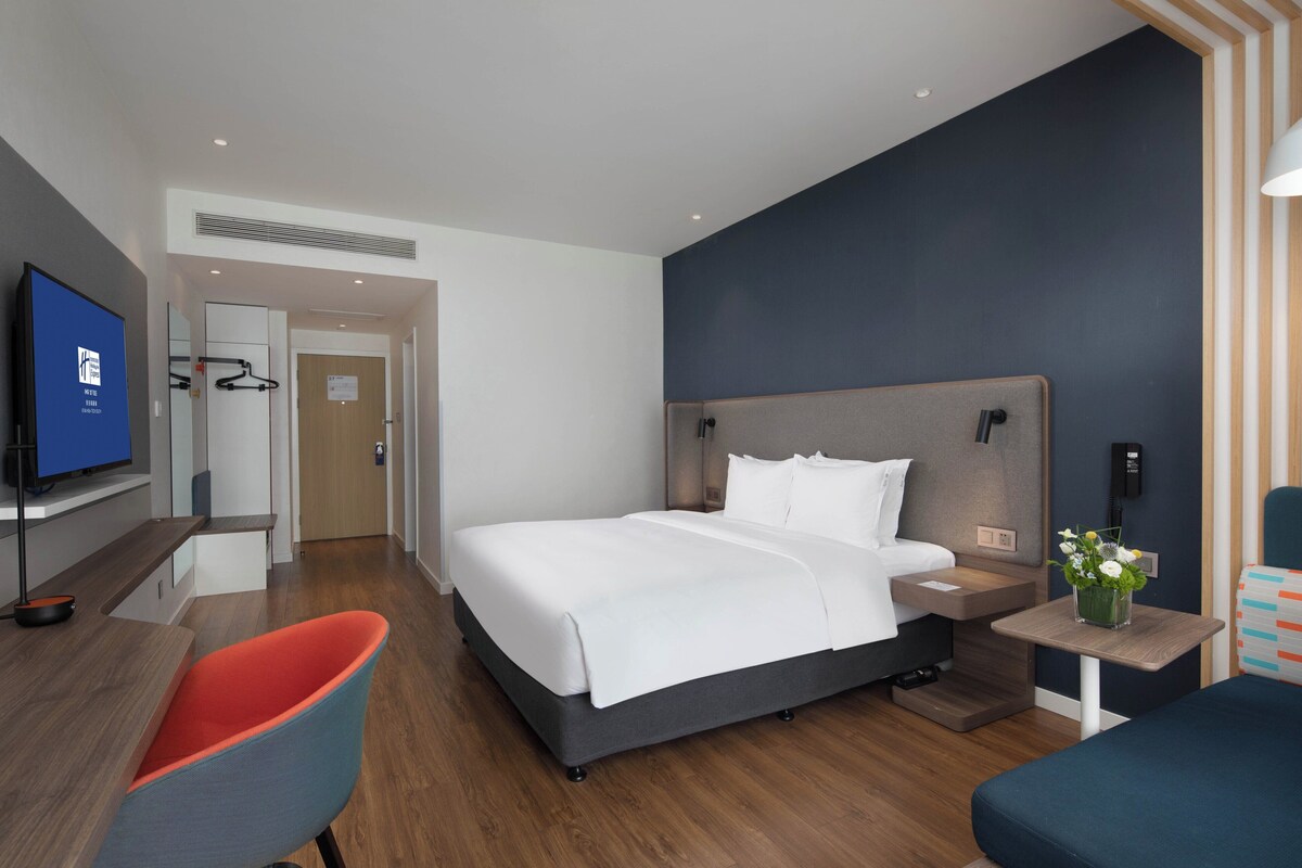 Ett modernt hotellrum med en stor säng, ett skrivbord, en stol och en tv.