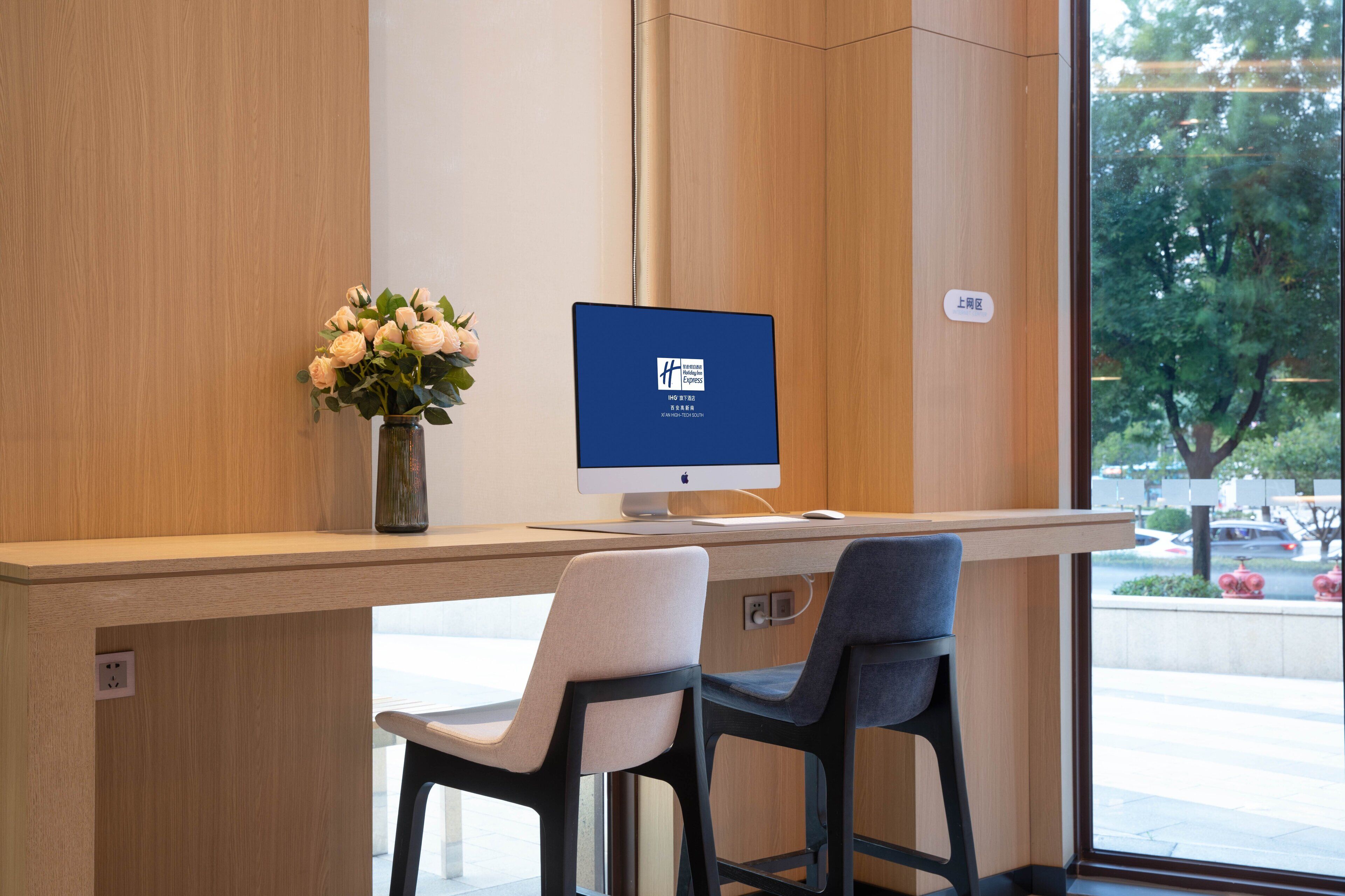 Un mostrador de recepción con un monitor de computadora, un florero con flores y dos sillas.