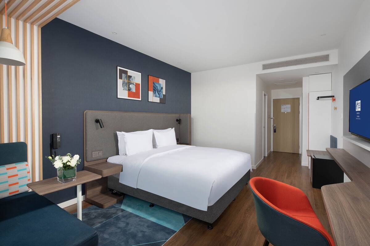 A modern hotel room with a large bed, a desk, a chair, and a TV.