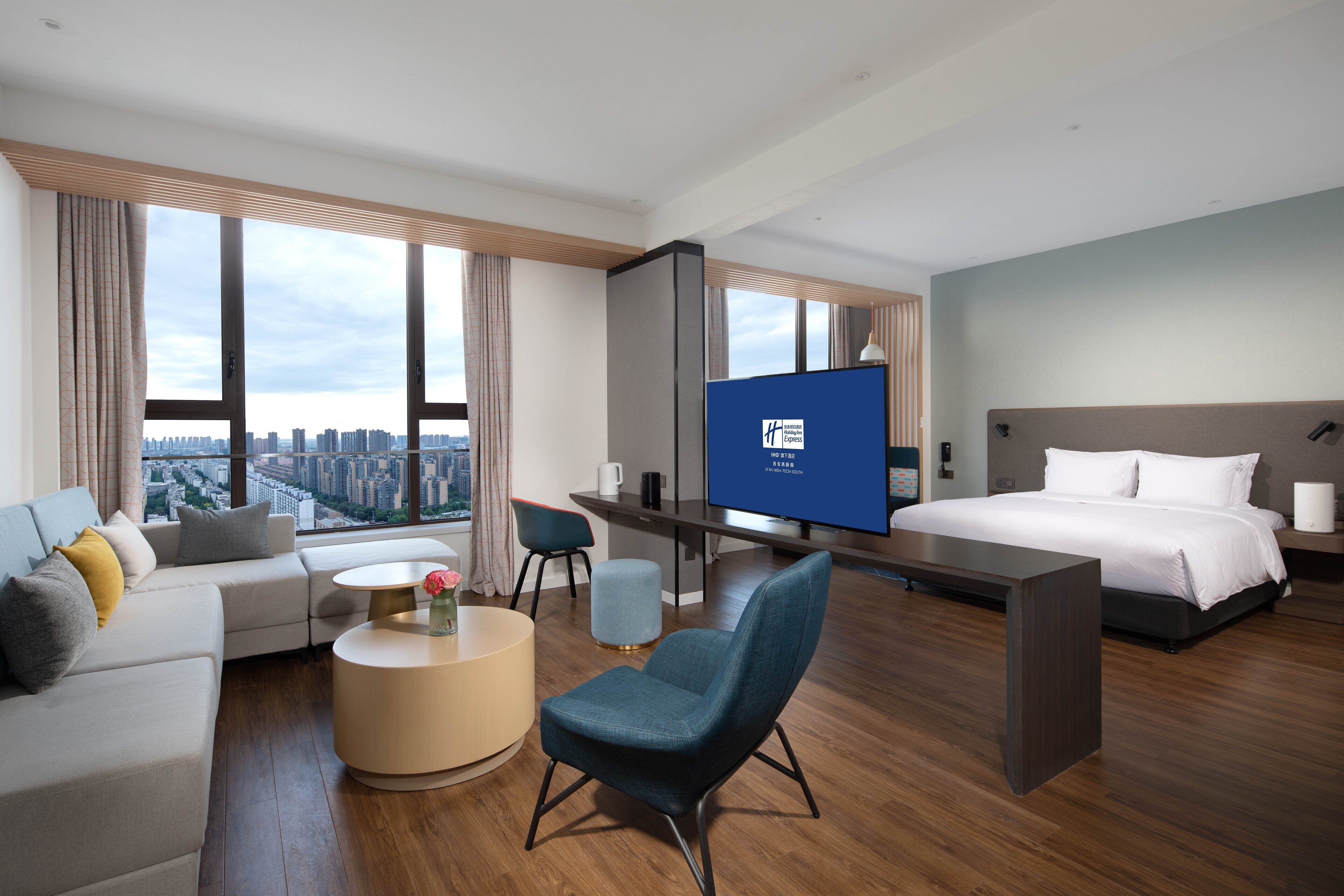 A modern hotel room with a large bed, a desk, a sofa, and a TV.
