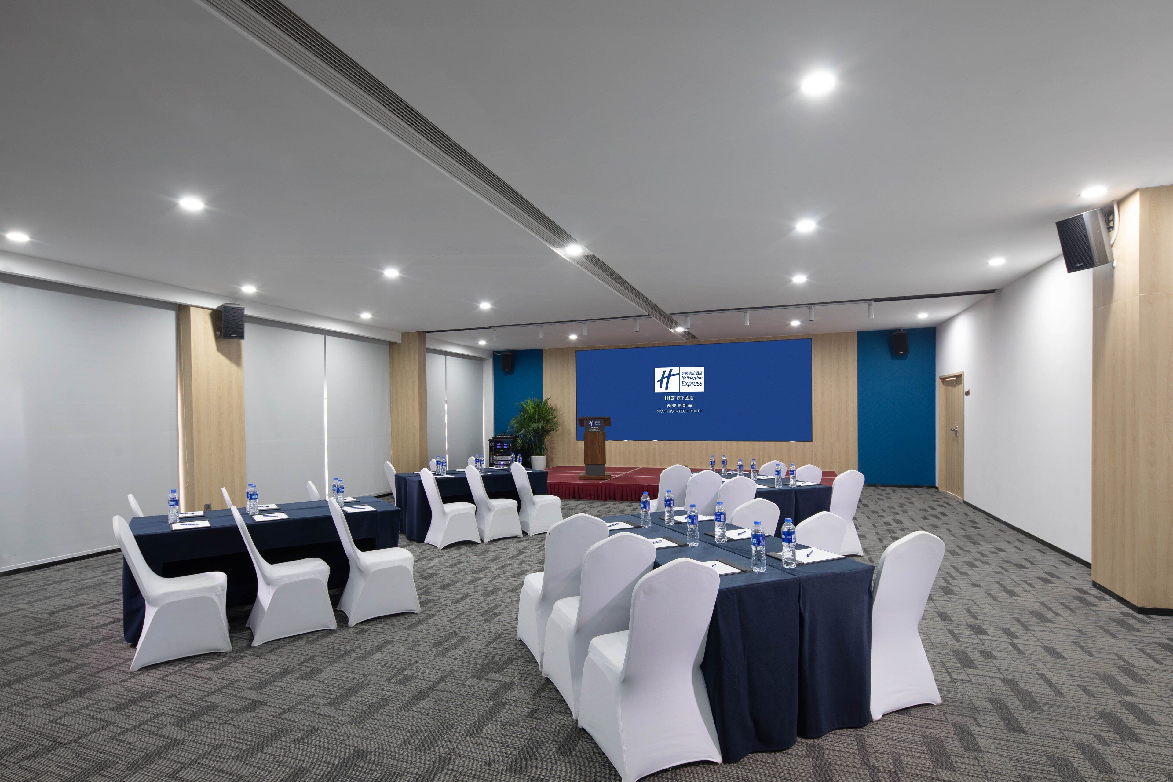 Uma sala de conferências com mesas, cadeiras e uma tela de projeção.