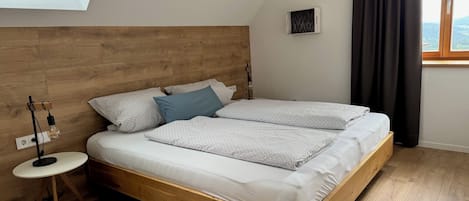 Un dormitorio con cabecera de madera, tragaluz, mesita de noche con lámpara y vistas al exterior a través de una ventana.