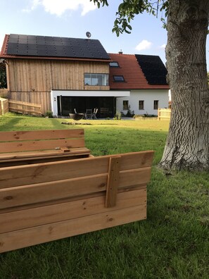 Uma casa moderna com telhado solar, deck de madeira e uma grande árvore.