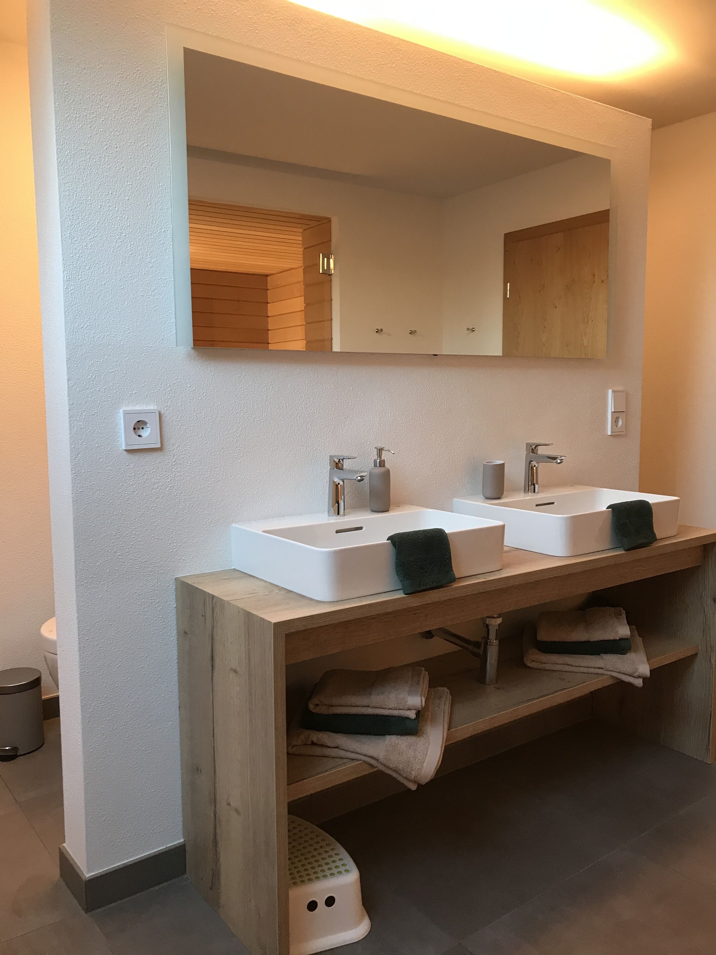 A modern bathroom with two sinks, a mirror, and wooden shelves.