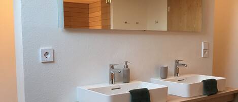 A modern bathroom with two sinks, a mirror, and wooden shelves.
