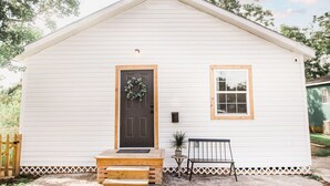 A small, single-story house with a dark front door, a small window, and a porch with steps and a bench.
