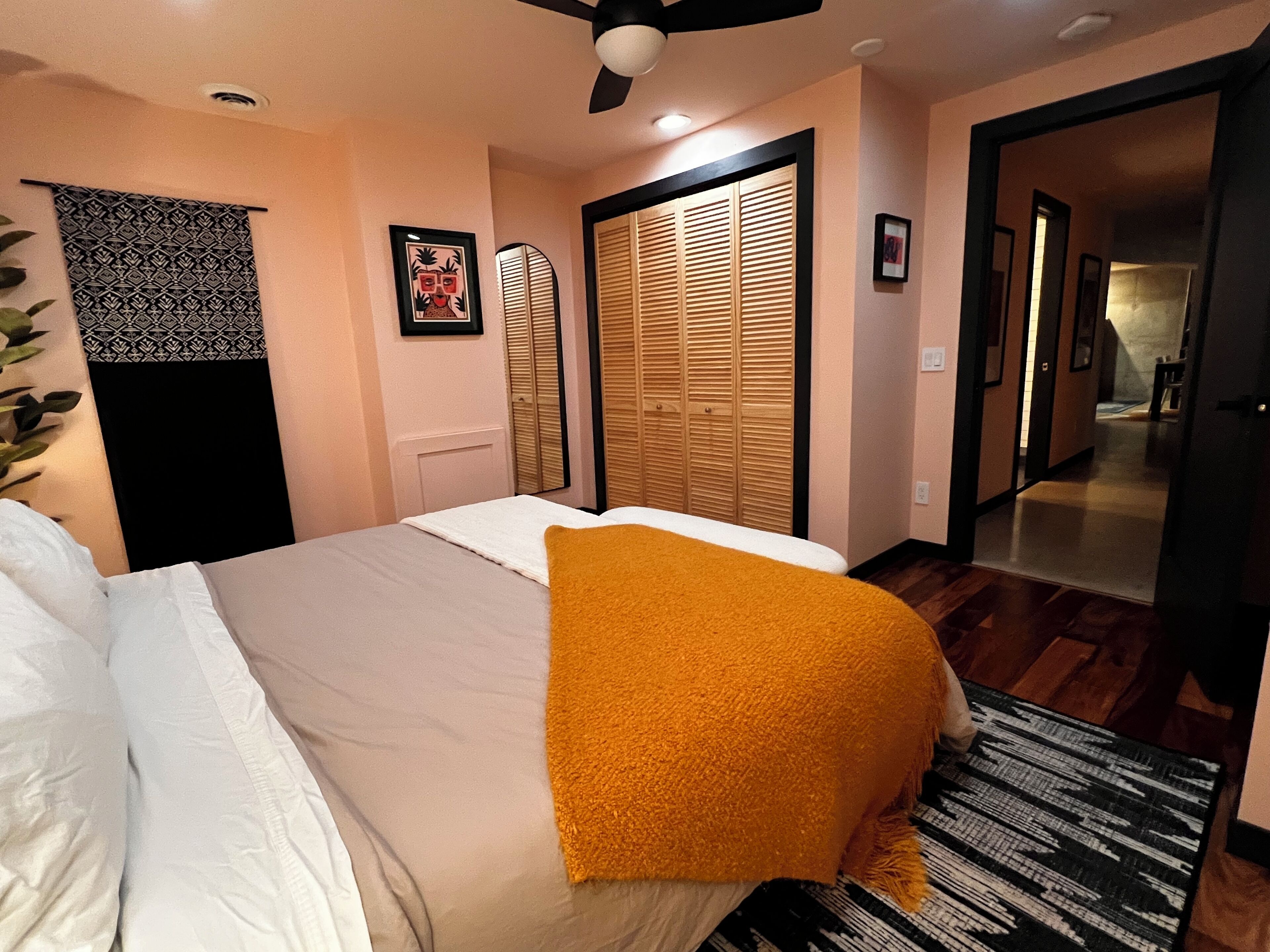 A bedroom with a bed, a ceiling fan, a wooden wardrobe, and a door leading to another room.