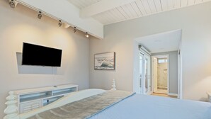 Un dormitorio moderno con una cama grande, un televisor montado en la pared, un cuadro y un baño visible a través de una puerta abierta.