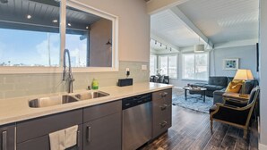Una cocina moderna con un ventanal grande, electrodomésticos de acero inoxidable y una zona de comedor con sofá y mesa de centro.