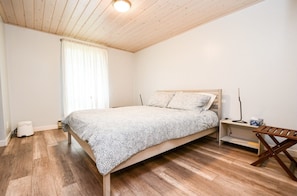 A bedroom with a wooden bed, a bedside table, a bench, and a window with curtains.