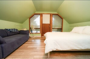 Cozy loft-style room with a bed and sofa, featuring a wooden door and a standing fan.