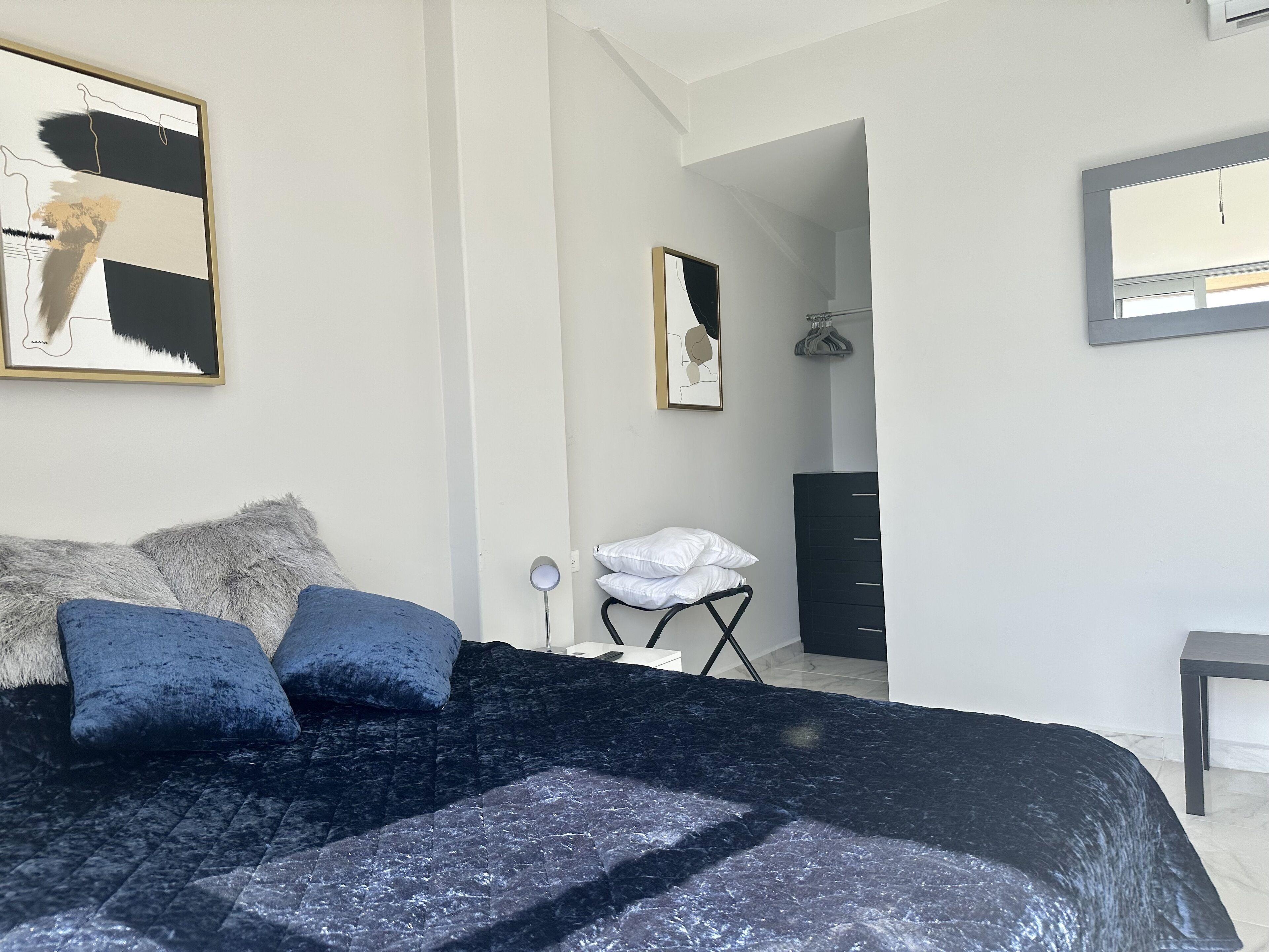 Un dormitorio con cama, almohadas, cómoda y obras de arte en las paredes.