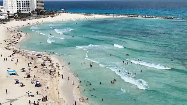 A beach with clear turquoise waters, a sandy shore, and a few buildings in the background. - Beachfront PENTHOUSE - Best Views + 3-Beds + 2 Balconies + Maid Service (Cancún)