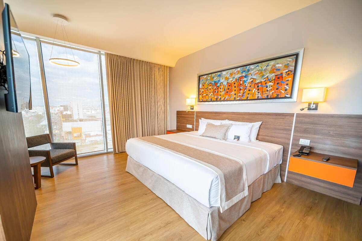 Habitación de hotel con una cama grande, un escritorio, una silla, un cuadro en la pared y vistas por la ventana.