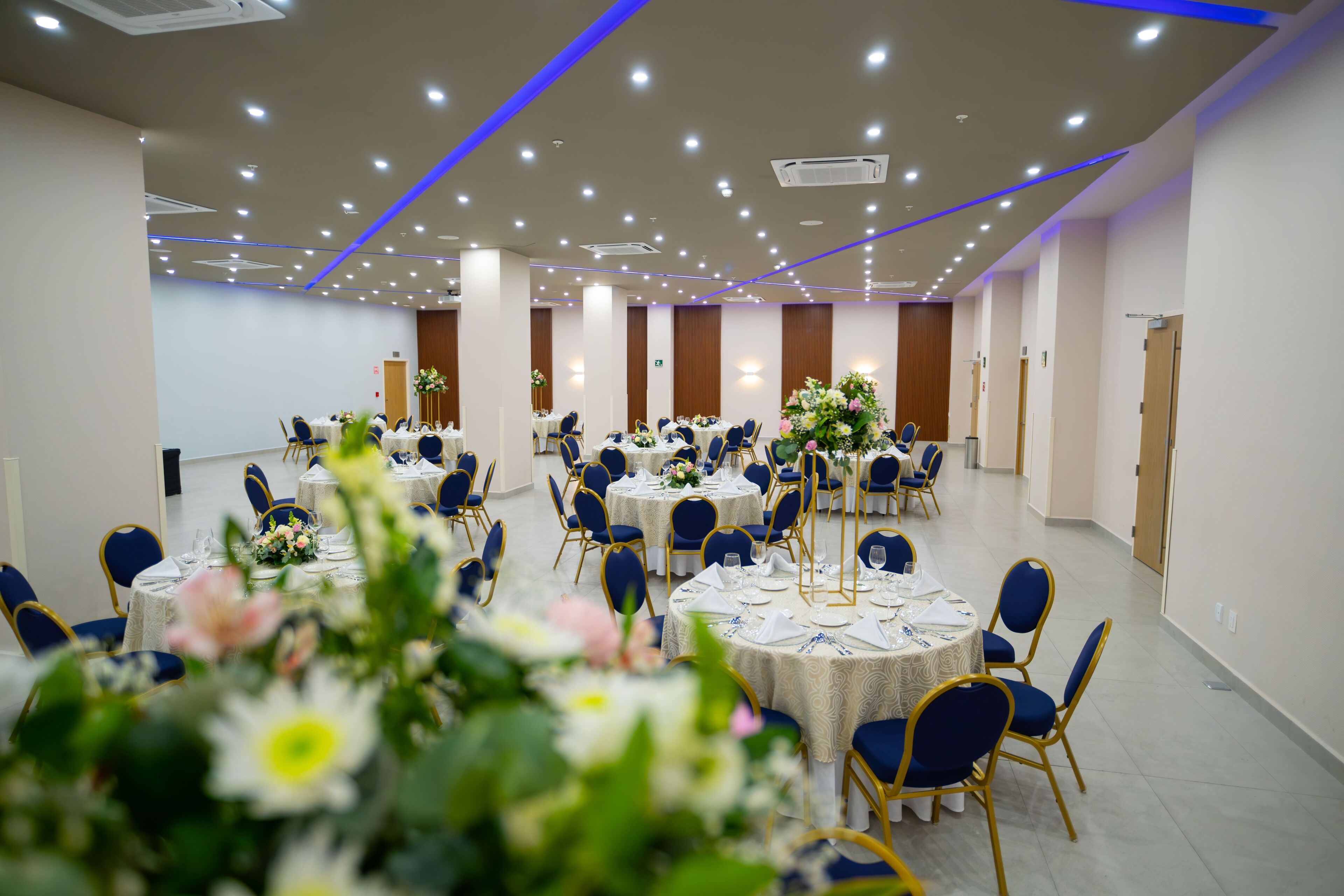 A banquet hall with round tables, blue chairs, and floral centerpieces.