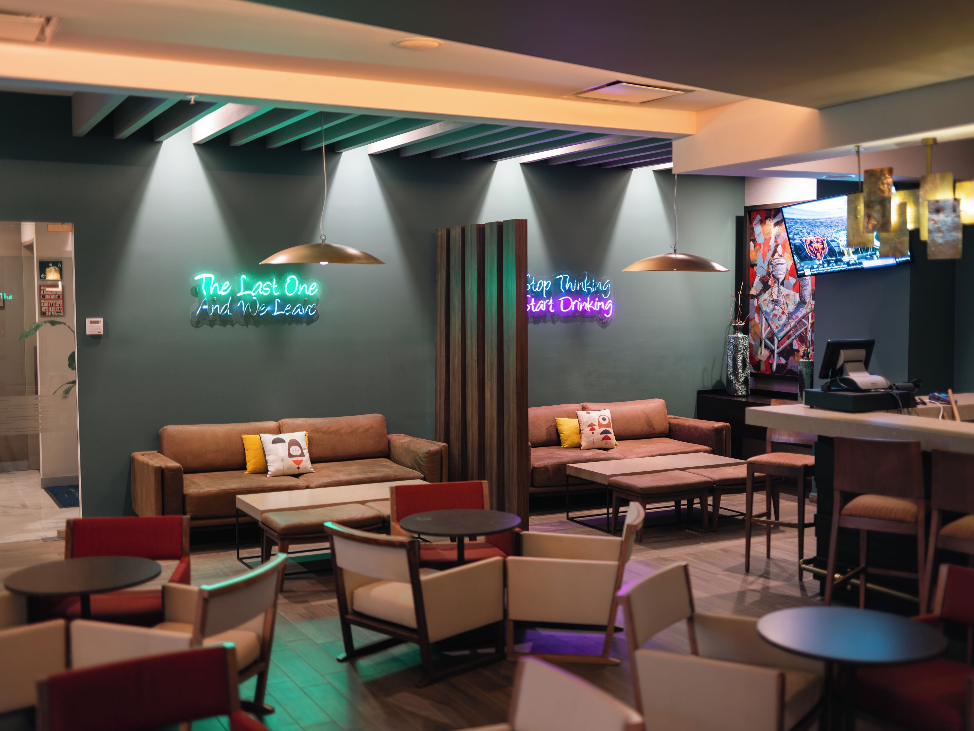 A modern lounge area with sofas, chairs, and tables, featuring neon signs and a television.