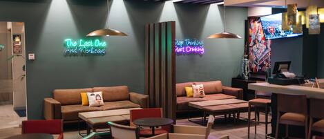 A modern lounge area with sofas, chairs, and tables, featuring neon signs and a television.