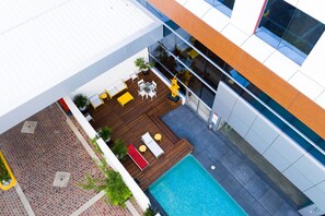 A rooftop pool area with wooden decking, lounge chairs, and a small table. - Metria Hotel (León)