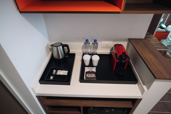 A kitchenette with a coffee maker, two bottles of water, two cups, a red electric kettle, and a packet of coffee creamer. - Metria Hotel (León)