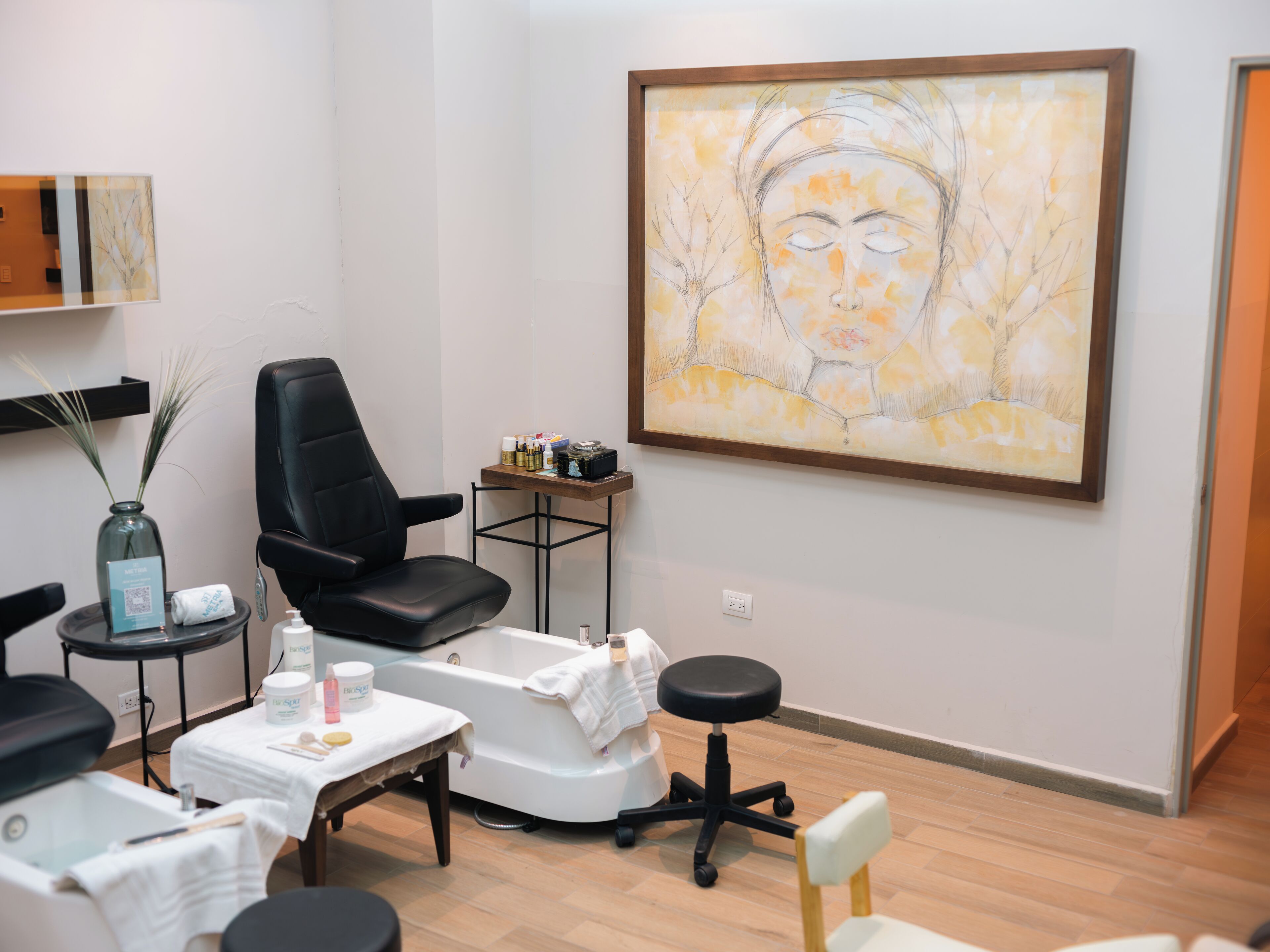 A modern spa room with a black leather chair, a white massage table, and a wooden floor.