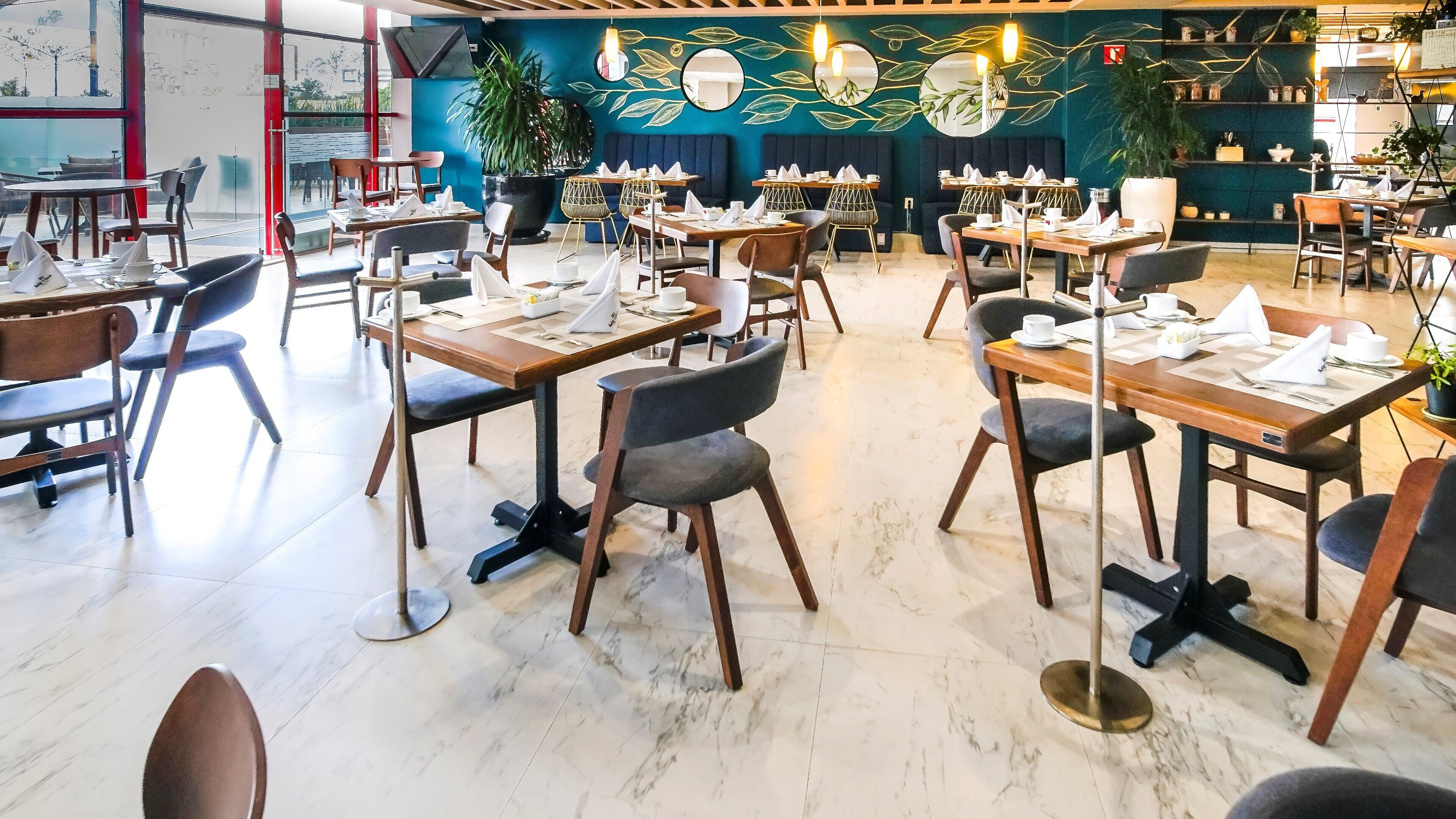 Un restaurant doté de nombreuses tables et chaises, d’un sol en marbre et d’un mur décoré de motifs représentant des feuilles.