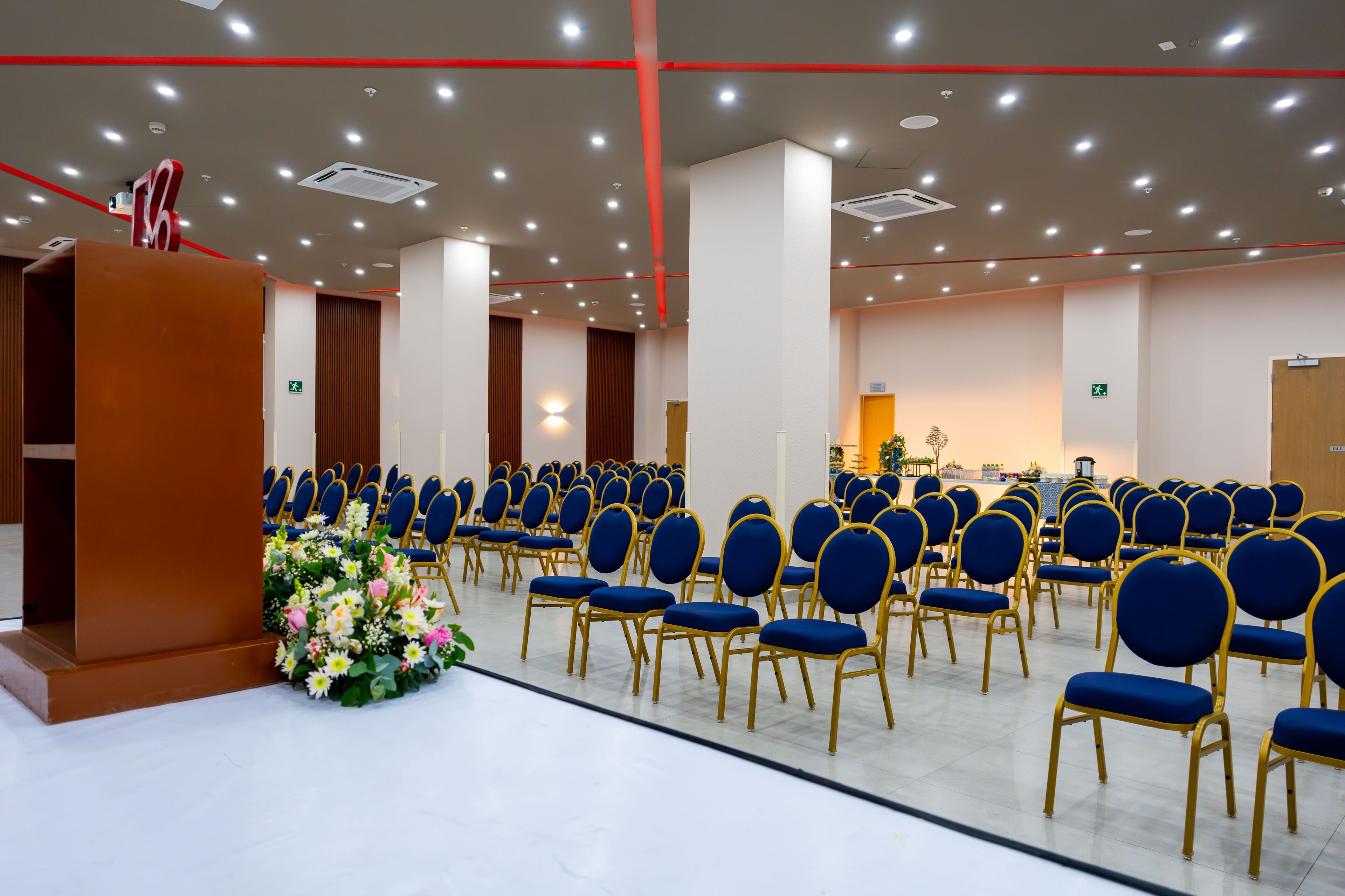 Un salón de conferencias con filas de sillas azules, un atril y un arreglo floral.