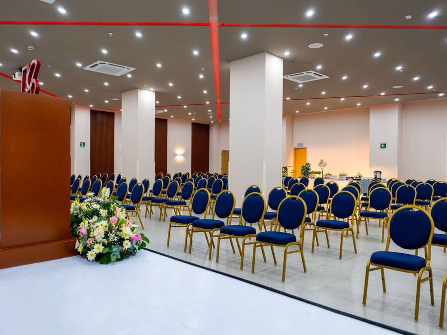 Un salón de conferencias con filas de sillas azules, un atril y un arreglo floral.