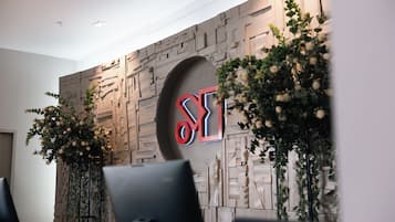 Una recepción moderna con un diseño geométrico en la pared, un logotipo destacado y dos grandes arreglos florales.