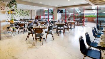 Un restaurante espacioso con varias zonas de comedor, mobiliario moderno y grandes ventanales que ofrecen vistas al exterior.