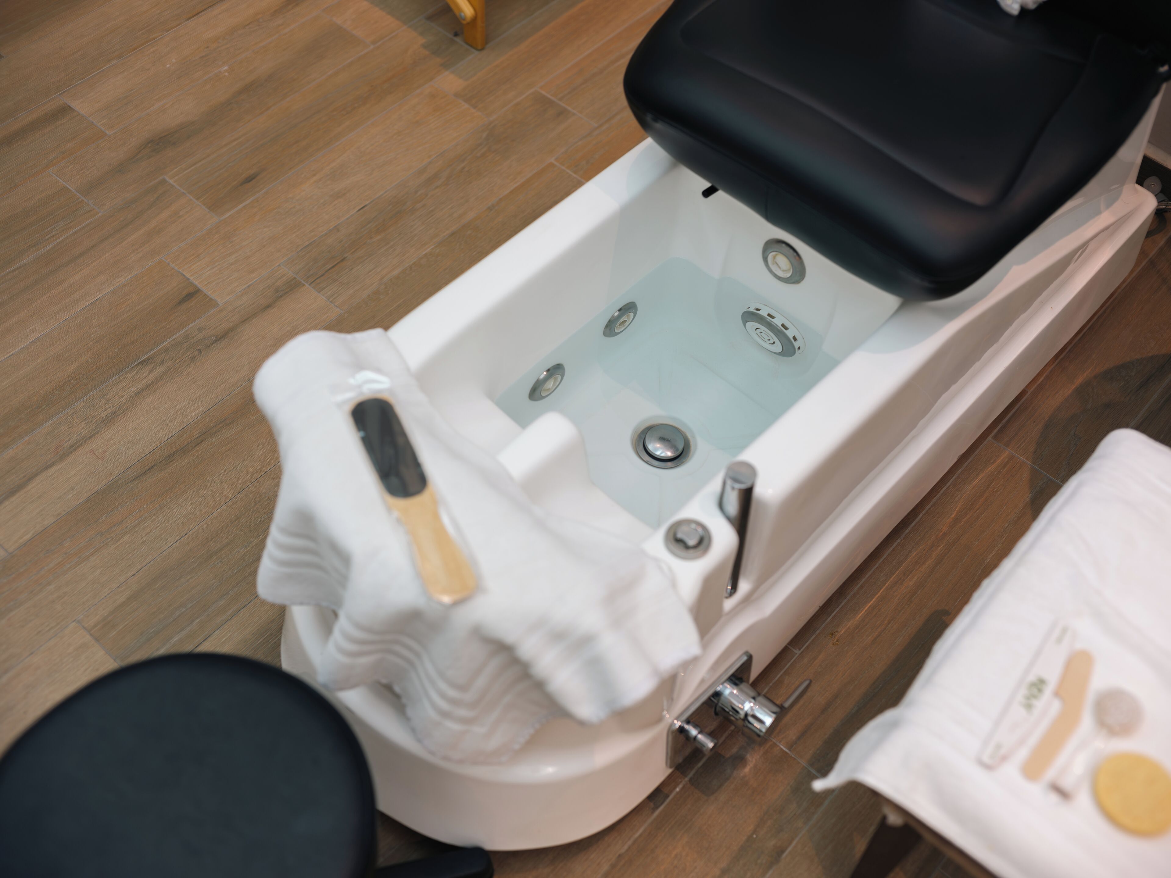 A bathtub with a black seat, a white towel, and a bottle of shampoo.